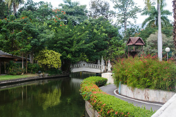Fototapeta na wymiar Buak Hard's lake, bird house and bridge surrounded by lush green vegetation, in Chiang Mai's old city public park