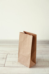 Paper bag on light wooden floor. Simple brown paper bag for lunch or meal. The layout for the design. Environmental ship packages.
