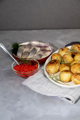 Boiled and roasted young potatoes, red caviar in a transparent scallop, herring sliced.