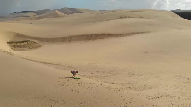 Man crashing while standing on a bodyboard and riding down the steep face of a sand dune in the desert