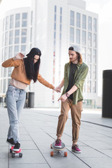 Fototapeta premium handsome man holding hands with brunette woman, pointing finger at skateboard