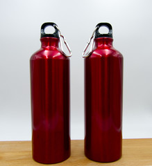 Two modern red water bottles on wooden table, white background