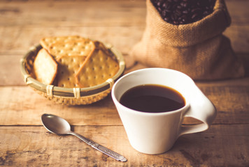 Black coffee In the cup white have roasted coffee beans are In a cloth bag sack butter cracker In...