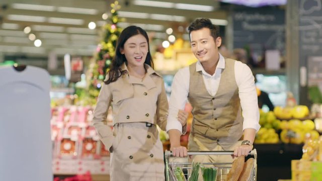happy young asian couple doing grocery shopping in supermarket