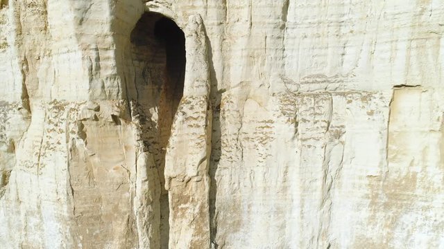 Close-up of relief white cliff slope and large grotto in the middle of slope. Shot. Majestic mountain cliff
