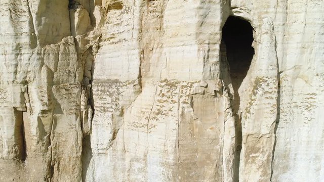 Close-up of relief white cliff slope and large grotto in the middle of slope. Shot. Majestic mountain cliff