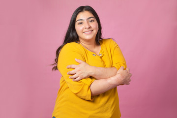 Chubby woman hugging herself transmitting self love with pink background