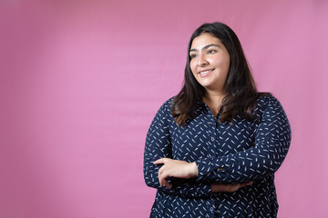 Curvy woman with arms crossed smiling with a pink background