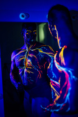 UV patterns body art of the circulatory system on a man's body. On the chest of a muscular athlete, veins and arteries are drawn with fluorescent dyes. Bodybuilder is standing at the mirror.