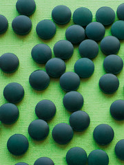 Spirulina algae tablets on green background from top view