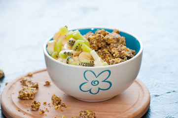 Healthy breakfast of granola, kiwi, banana and yogurt in a bowl on a wooden tray. Fitness diet for weight loss