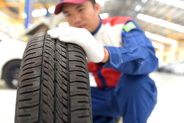 Fototapeta na wymiar Handsome young auto mechanic in uniform is examining a tire while working in auto service Mechanic holding a tire tire at the repair garage replacement of winter and summer tires.