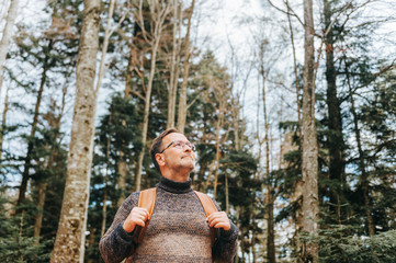 Handsome middle age man hiking in forest, wearing pullover, backpack and glasses