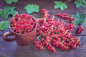 red currant in a ceramic Cup and bunches of berries on the table close-up. background with red currant and leaves