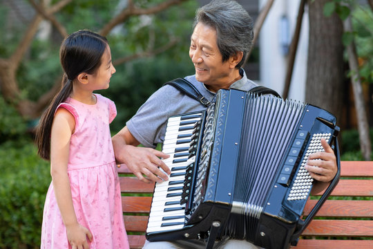Happy grandfather and granddaughter playing accordion