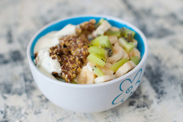 Granola, kiwi, banana and Greek yogurt in bowl, a plate on a gray concrete background, close-up view from the top. Fitness diet for weight loss and proper nutrition