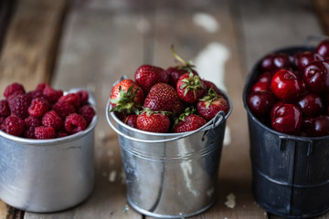 harvest of summer berries. Strawberries, cherries, raspberries in pails on a wooden table. Country style