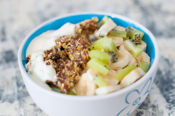 Granola, kiwi, banana and Greek yogurt in bowl, a plate on a gray concrete background, close-up view from the top. Fitness diet for weight loss and proper nutrition