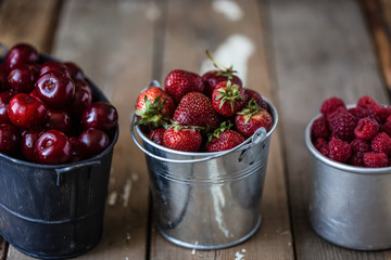 harvest of summer berries. Strawberries, cherries, raspberries in pails on a wooden table. Country style
