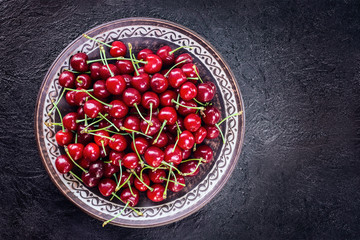 cherry berries in a plate on a dark background top view. copy space. cherry flat lay. ripe cherries background