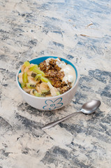 Granola, kiwi, banana and Greek yogurt in bowl with a spoon on a gray concrete background, copy space. Fitness diet for weight loss, proper nutrition and a healthy lifestyle