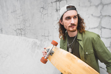 calm man looking away, standing near wall with skateboard © LIGHTFIELD STUDIOS