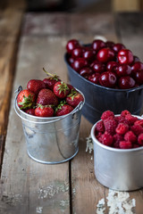 harvest of summer berries. Strawberries, cherries, raspberries in pails on a wooden table. Country style