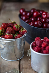harvest of summer berries. Strawberries, cherries, raspberries in pails on a wooden table. Country style