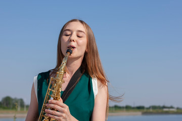 Beautiful smiling girl with saxophone. Young beautiful saxophonist with saxophone - outdoor in...
