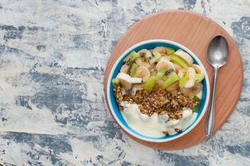 Greek yogurt, granola, kiwi and a banana in bowl with a spoon on a gray concrete background, wooden tray, copy space view from the top. Fitness diet for weight loss, proper and tasty food