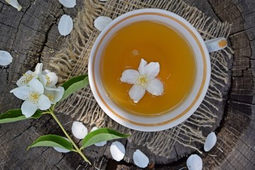 Jasmine flowers and fresh tea on wooden background and burlap.