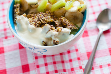 Granola with Greek yogurt kiwi and banana in bowl on a pink napkin, close-up view from the top. Fitness diet for weight loss, proper and tasty food