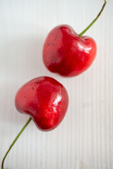 Top view of two cherries diagonally on white wooden background in vertical