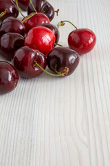 Top view of cherries on white wooden background in vertical with copy space
