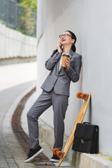 cheerful businesswoman in formal wear standing near skateboard, talking at smartphone