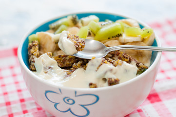 Granola with Greek yogurt kiwi and banana in bowl on a pink napkin, close-up. Piece of dessert on a spoon. Fitness diet for weight loss, proper and tasty food