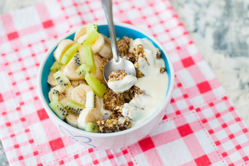 Granola with Greek yogurt kiwi and banana in bowl on a pink napkin, view from the top. A piece of dessert on a spoon. Fitness diet for weight loss, proper and tasty food