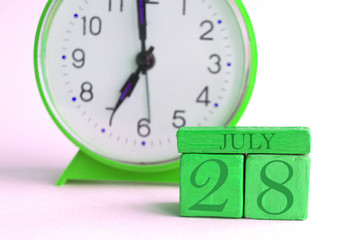 july 28th. Day 28 of month, handmade wood calendar and alarm clock on light green color. summer month, day of the year concept