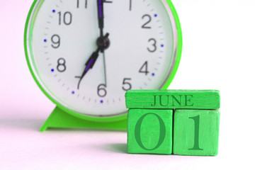 june 1st. Day 1 of month, handmade wood calendar and alarm clock on light green color. summer month, day of the year concept