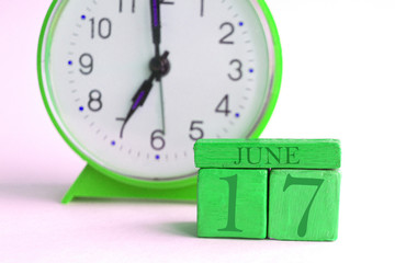 june 17th. Day 17 of month, handmade wood calendar and alarm clock on light green color. summer month, day of the year concept
