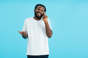 african american man with shrug gesture talking on smartphone, isolated on blue