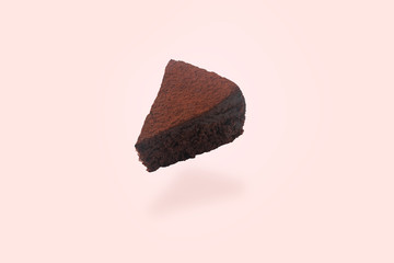 levitating piece of chocolate cake with cocoa powder on top over pink background