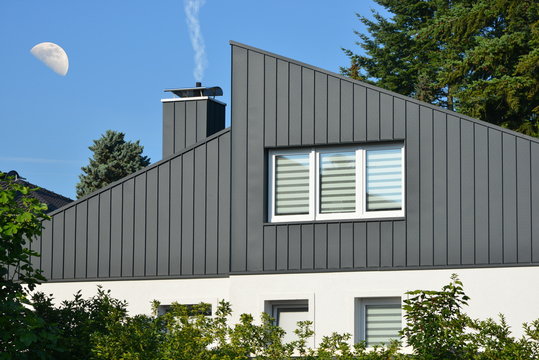 Fassaden- und Schornstein-Verkleidung eines modernen Wohngeb&auml;udes aus dunkelgrau beschichtetem Stehfalz-Metall und Fenster mit Sichtschutzstreifen, 