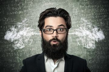 bearded man with smoke coming out from his ears, over blackboard inscribed with scientific formulas and calculations in physics and mathematics, concept tired student or young teacher