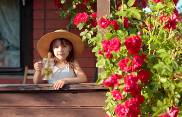 Portrait of little girl in straw hat with glass of herbal tea.