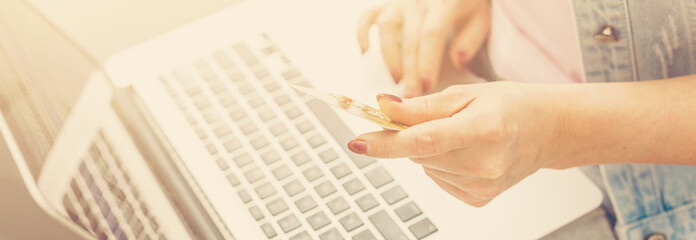 Fototapeta premium Woman is holding credit card and using laptop computer. Online shopping concept. Close up.