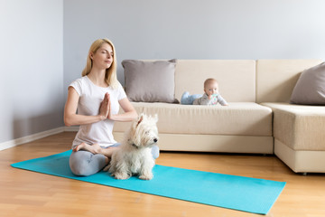 Mother and child with white dog in a bright room with grey walls and wooden floor on blue mat exercising yoga calm fitness white sofa counch in home 