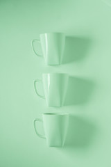 3 green coffee mugs on green background in a vertical row with empty copyspace