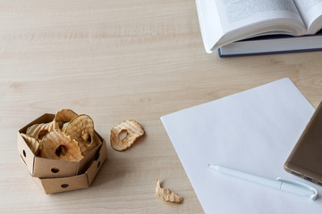 Healthy homemade dried apple chips snack in the beeswax wraps box on the school table with book, pan and white paper copy space.