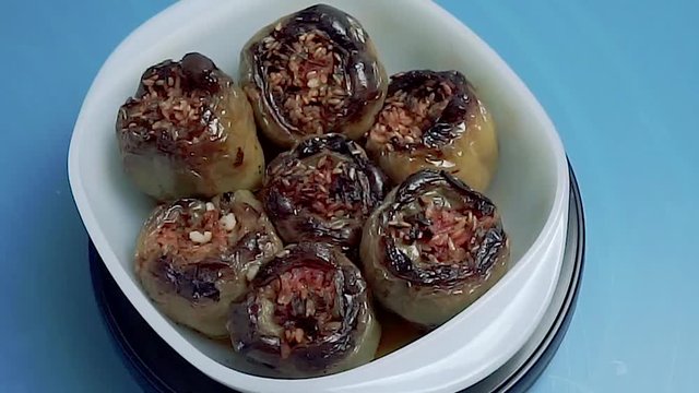 Stuffed green peppers rotating on blue background. Cooked traditional Turkish meal in white plate
